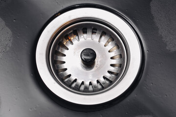 Metal sink drain close up. Stainless steel circular strainer. Wet black surface around. Home...