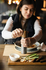 A woman in a restaurant adds pepper or salt to her dish.