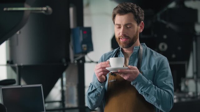 Smiling Caucasian man small business owner barista smell coffee beans roasted holding cappuccino cup espresso smelling fresh aroma caffeine roasting factory male worker serving order in coffeehouse