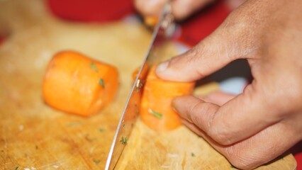 Close-up of hands slicing fresh carrots on a wooden cutting board with a kitchen knife.