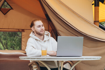 Cute happy freelancer guy using laptop away from the city on a campsite.