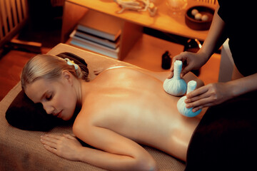 Hot herbal ball spa massage body treatment, masseur gently compresses herb bag on woman body....