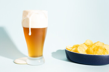 Overflowing beer with foam and snack on light backdrop