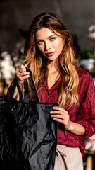 Fototapeta premium A girl stands outdoors, holding a black reusable shopping bag, emphasizing sustainable living and conscious consumption.