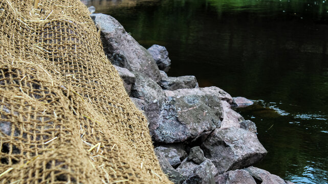 close-up of a bank stabilization project along a creek. watershed restoration with riprap and an erosion control blanket.