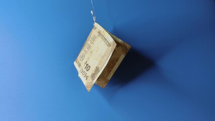 Indian rupee money or currency note hooked on fishing hook like lure or bait Isolated against a blue background with copy space. debt, scam, rat race, phishing, financial trap and inflation concept.