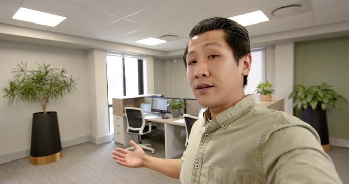 Gesturing Asian man in business attire presenting computer monitors in office, copy space
