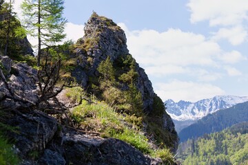 A rocky peak with vegetation rises against a partly cloudy sky, with snowy mountains in the distance in Zakopane - Lesser Poland - Poland