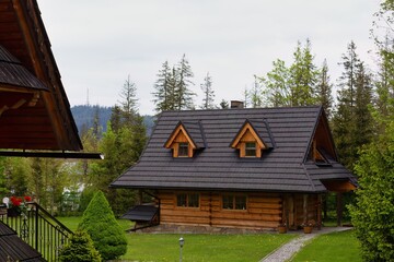A wooden cabin in a clearing, surrounded by lush forest. The cabin has a dark roof with two dormer windows and a stone chimney in Zakopane - Lesser Poland - Poland