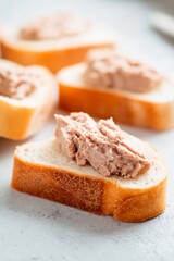 Slices of soft bread are generously spread with a savory p&acirc;t&eacute;, arranged neatly on a clean countertop. This simple yet tasty snack offers a delightful flavor combination