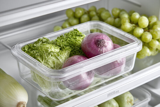 Crisp lettuce, onions, and green grapes arranged in a clear container inside a refrigerator, showcasing freshness