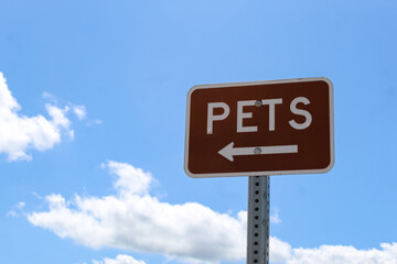 A sign indicating the way to a designated pet walking area isolated against a blue sky.