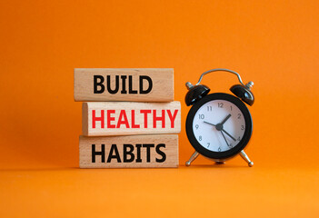 Healthy habits symbol. Concept word Build Healthy habits on wooden blocks with alarm clock....