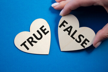 True or False symbol. Concept word True or False on wooden hearts. Businessman hand. Beautiful blue...