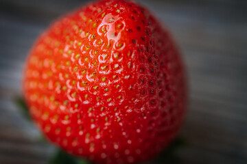 Macro image of a bright red, ripe strawberry lying on a rustic wooden surface, with visible seeds...