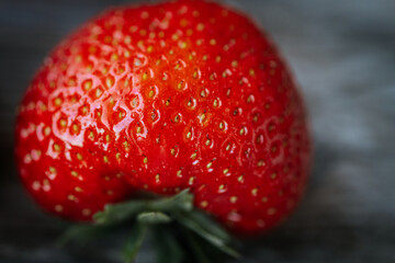 Macro image of a bright red, ripe strawberry lying on a rustic wooden surface, with visible seeds...