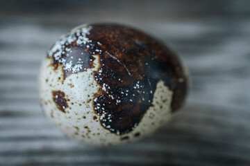 A detailed close-up of a quail egg with dark brown and white mottled patterns, placed on a rustic...