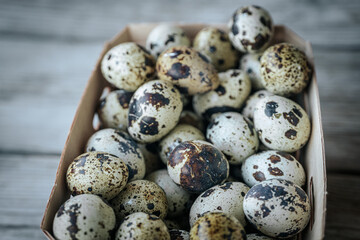 Fototapeta premium A close-up of a cardboard box filled with colorful quail eggs, revealing their natural patterns and textures. A rustic wooden backdrop enhances the organic appeal.