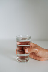A hand reaches for a glass of water on a white surface, emphasizing daily hydration.
