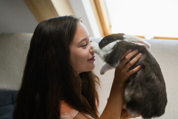 Girl holding rabbit touching noses in cozy room.