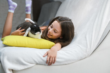 Girl lying on sofa and hugging rabbit on pillow.