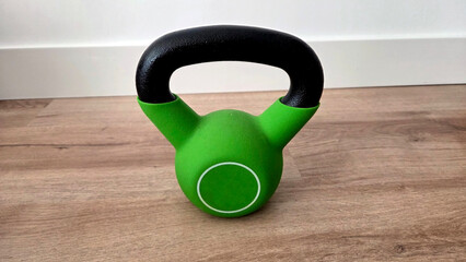 Green kettlebell on wooden floor for home fitness and strength training. Healthy lifestyle, sport...