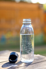 Open transparent bottle of clean mineral water outdoors in the garden on a wooden table. Drinking regime on hot summer days