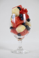 Watermelon and melon cubes, and blueberry in a glass on a light background