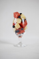 Watermelon and melon cubes, and blueberry in a glass on a light background
