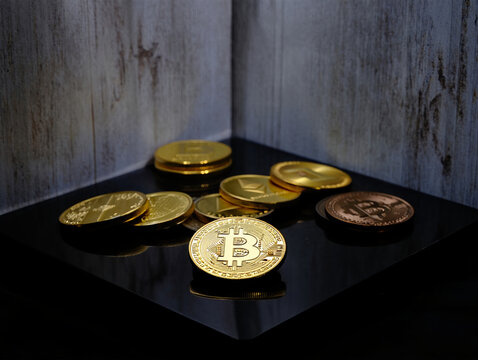 A collection of gold bitcoin coins are scattered on a dark reflective surface