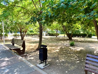 Serene park setting with wooden benches under lush green trees, providing peaceful environment for...