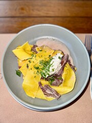 A delectable presentation of pasta with tenderly cooked meat, topped with herbs and cream, served in a bowl on wooden table, radiating gourmet quality and culinary sophistication.