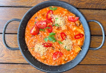 Freshly prepared tomato-based risotto served in black pan, garnished with red chili slices, fresh parsley, sprinkled with parmesan. Ideal for illustrating Italian cuisine concepts and appetizing meals