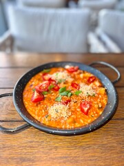Vibrant tomato-based risotto featuring cherry tomatoes and fresh herbs served in rustic bowl on wooden table. Hearty, visually appealing dish perfect for food photography and culinary presentations.