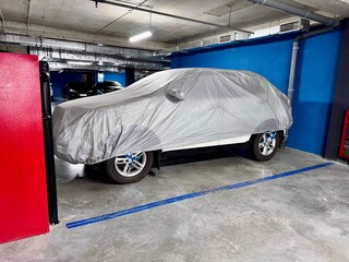 A vehicle securely covered with a protective sheet in an underground parking garage. A blue wall,...