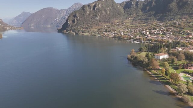 Drone shot of Lake Idro with mountains, colorful buildings, and clear blue water beside autumn trees