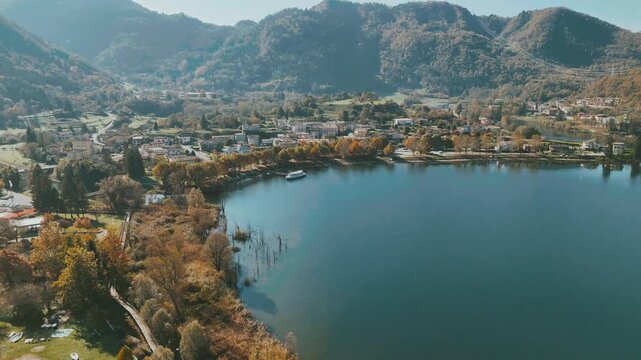Drone shot of a Idro lakeside town surrounded by forested hills and autumn trees