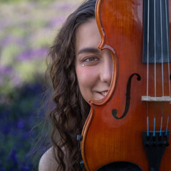 A beautiful young violinist, female with long hair with her viola near face, in an outdoor setting...