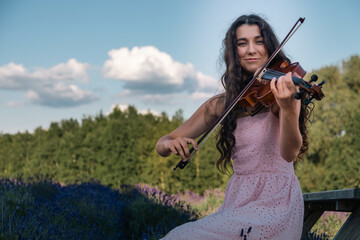 A beautiful violinist, young female with long hair plays her viola in lavender field. Music artist...