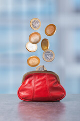 Red purse with coins floating above in bright indoor location during daytime creates a sense of financial opportunity