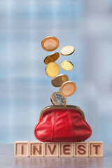 Coins flowing from a red wallet above investment blocks signify financial growth and saving strategy in a minimalist setting