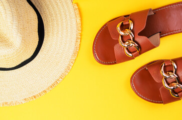 Top view of summer slippers and beach hat on bright yellow background