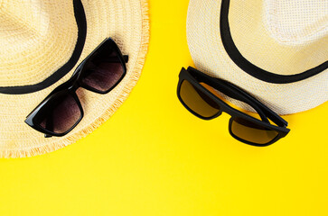 Two light beach hats with two sunglasses on yellow summer background