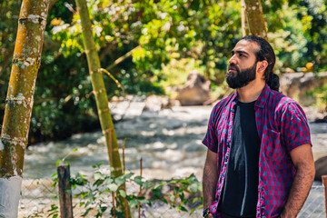 Obraz premium Contemplative Colombian man in plaid shirt standing in nature-rich forest setting near river at Santuario, Risaralda, Colombia with copy-space and rustic background