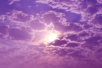 Purple golden yellow orange sky and white cumulus cloud with sunlight shining through. Sunset sunrise cloudscape sky.