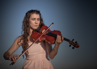 A beautiful young female with long hair violinist plays her viola in an outdoor setting, against...