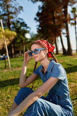 Modern boho-western denim street style woman wearing blue sunglasses and red headscarf sitting...