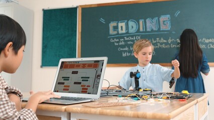 Asian boy coding program while caucasian friend fixing electric board at STEM class. Energetic student standing blackboard while writing coding engineering prompt and programing AI software. Pedagogy.