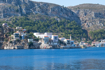 Naklejka premium This photo reflects the charm of Meis Island bathed in sunlight, showing colorful beach houses nestled against rocky cliffs and calm blue waters.