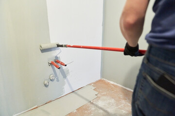 A man paints walls with a roller, working painting on the surface, painting walls in an apartment,...